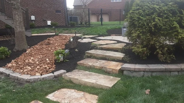 Flagstone steps set into a lawn beside a dry creek bed of river rock, fresh black mulch and a low stone retaining wall, at a brick house